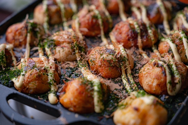 鉄板の上でソースとマヨネーズ、青のりをかけた焼きたてのたこ焼き