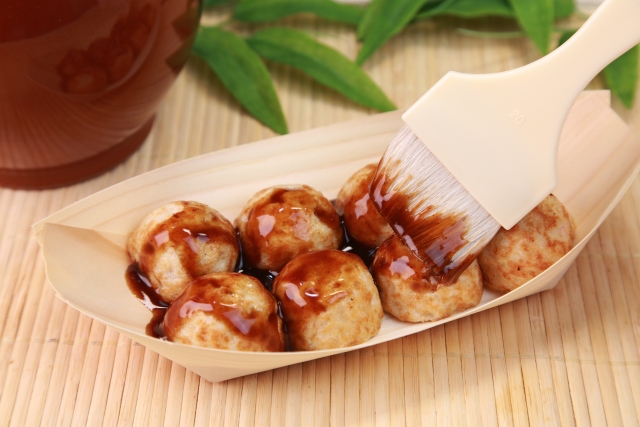 舟形の容器に入ったたこ焼きに刷毛でソースを塗っているところ