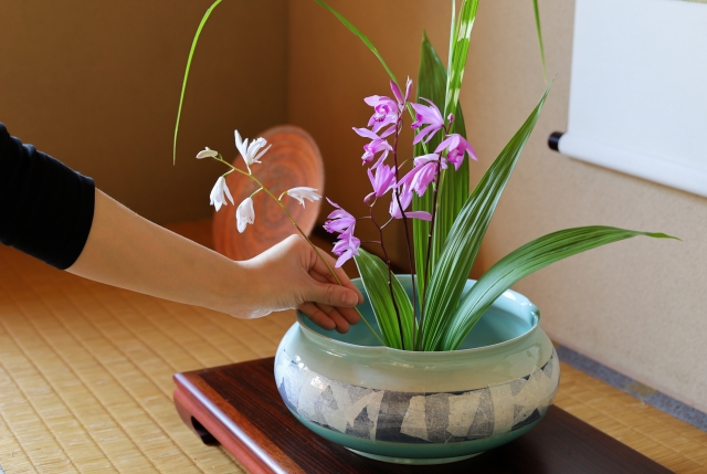 水盤に紫の花と葉を生けている手元
