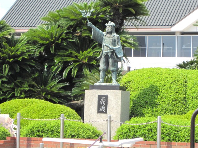 植え込みの中の台座の上で、采配を掲げる大石内蔵助の銅像